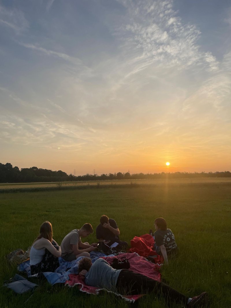 Jugendliche sitzen bei Sonnenuntergang auf Decken in einer Wiese